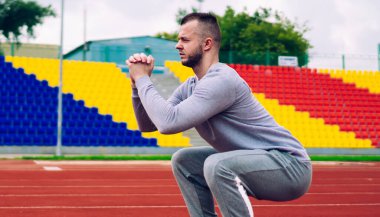 Stadyumda Tribün 'e karşı atlama egzersizleri yaparken eşofmanlı ve spor ayakkabılı kararlı güçlü antrenörün yan görüntüsü.