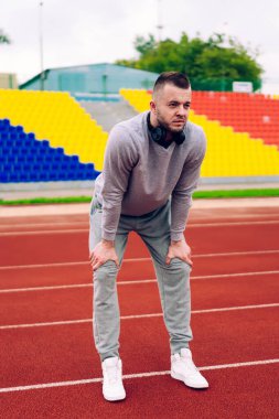 Eşofmanlı, kulaklıklı, stadyum pistinde dinlenen ve gözlerini kaçıran bir sürü konsantre genç adam.