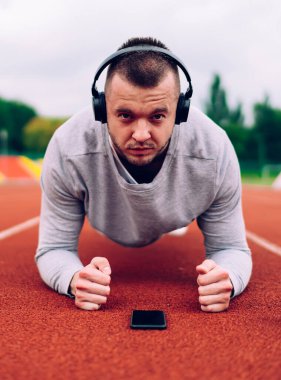 Kulaklıklı güçlü, kararlı, beyaz bir adamın portresi. Radyoyu dinliyor. tahtada duruyor, ciddi bir erkek atlet kamera eğitimine bakıyor. Dayanıklılık ve kulaklıktaki kas gücü.