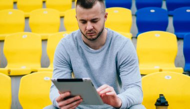 Ciddi erkek koşucu antrenman sonuçlarını dijital tablet ve 4G bağlantısı kullanarak kaydediyor. Eşofmanlı dalgın bir adam e-posta gönderiyor ve egzersiz ve egzersizler hakkında bilgi topluyor.