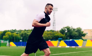 Hareketli yakışıklı adam stadyumun dışında koşuyor. Esneklik ve hedeflere ulaşmak için koşuyor. 20 'li yaşlarda erkek koşucu formda ve formda kalmak için sabah antrenmanı yapıyor.