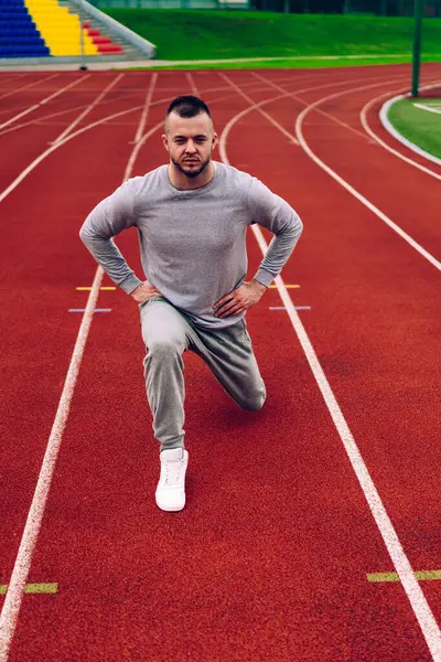 Spor kıyafetleri ve spor ayakkabıları giymiş sporcunun yukarıdan, stadyumda antrenman yaparken bacak egzersizi yapıyor.