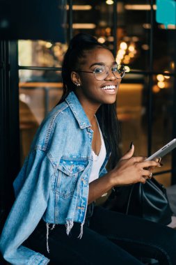 Gözlüklü, at kuyruklu ve kameraya gülümseyen neşeli Afro-Amerikan kadın manzarası.