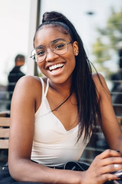 Mutlu gülümseyen Afro-Amerikan kadın tablet üzerinde internette sörf yaparken modern şehir kafeteryasının yaz bölgesinde oturuyor.