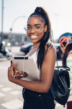 İyimser Afro-Amerikalı kadın, günlük giysiler içinde şehir caddesinde yürüyor, otoyolu geçiyor.