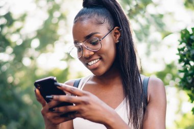 Güler yüzlü, koyu tenli, internetten rezervasyon yaptıran bir kadın akıllı telefonuyla parkta oturuyor, neşeli hippi kız boş zamanlarında cep telefonuna yeni bir uygulama yüklüyor.