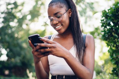 Güler yüzlü, koyu tenli, internetten rezervasyon yaptıran bir kadın akıllı telefonuyla parkta oturuyor, neşeli hippi kız boş zamanlarında cep telefonuna yeni bir uygulama yüklüyor.