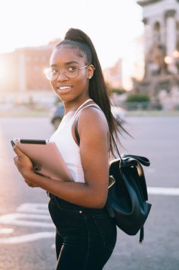 Şehre yakın bir yerde sırt çantalı ve tableti incelerken kameraya gülümseyen genç bir etnik kadın.