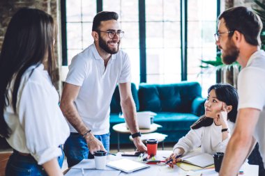 Erkek ve kadın yöneticiler pazarlama stratejisini tartışırken aynı zamanda tuğla duvarlar ve panoramik pencerelerle gün ışığında birlikte çalışıyorlar.
