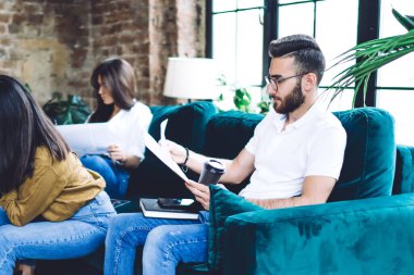 Rahat koltukta oturan ve modern ofiste gazetelerle çalışan gündelik kıyafetlerle odaklanmış iş arkadaşlarıyla dolu.