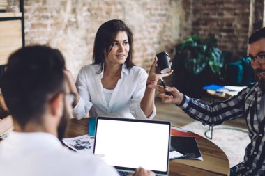 Bir grup içerikli çok ırklı iş arkadaşı, günlük kıyafetlerini giymiş, yuvarlak masada oturuyor ve ofis alanında iş planlarını tartışıyorlar.
