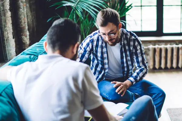 Erkek iş arkadaşlarının dokümanlarla birlikte çalıştığı yüksek açı, dizüstü bilgisayarlı ve kahveli koltuğun yanında otururken,