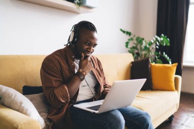 Ciddi bir erkek programcı kulaklıkla internet üzerinden webinar izleyip ev içi kablosuz internet bağlantısını kullanıyor. Modern dizüstü bilgisayarı olan kafası karışmış ve son teslim tarihi olan uzaktan kumandalı bir adam.