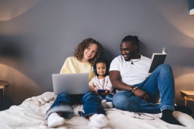 Neşeli anne dizüstü bilgisayar teknolojisi kullanırken baba kameraya gülümsüyor. Kulaklıklı tatlı çocuklarıyla birlikte. Mutlu bir evlilik portresi.