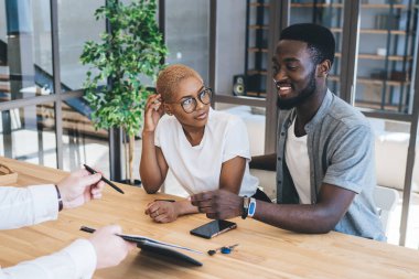 Yeni bir dairede resmi giysiler içinde oturmuş sözleşmeyi imzalamaya hazırlanan mutlu Afrikalı Amerikalı çift.