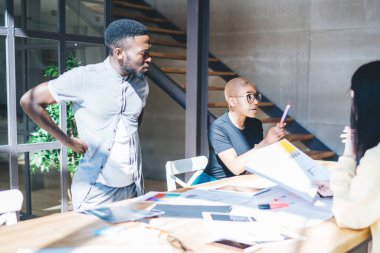 Çağdaş ofisteki iş toplantısı sırasında kağıtlardan elde edilen verileri analiz eden ve birbirleriyle konuşan bir grup çalışan.