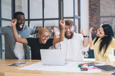 Muhteşem yaratıcı çok ırklı insanların oluşturduğu bir ekip laptopta el ele otururken ellerinde belgeler ve iş yerindeki renkli fosforlu kalemlerle birlikte oturuyor.