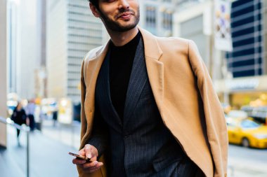 Deneyimli erkek girişimci zarif giyinmiş metropoliten şehir ortamında duruyor, resmi giyinmiş başarılı bir iş adamının modern akıllı telefon teknolojisini elinde tutarken görüntüsü.