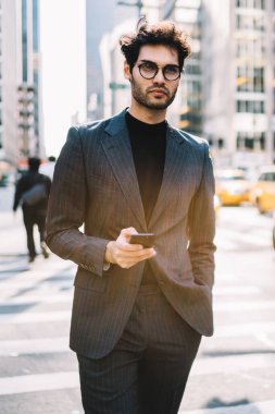 Klasik gözlüklü düşünceli bir adam modern cep telefonu teknolojisi üzerine iş yayınından gelen içerik metni üzerinde kafa yoruyor. Finans bölgesinde akıllı telefon kullanan genç Avrupalı erkek yönetmen.