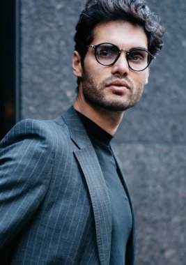 Yakışıklı Avrupalı girişimcinin yarı boy portresi lüks takım elbise ve görüş düzeltmesi için optik gözlük takmış finans bölgesindeki kameraya bakıyor, iş adamı şehir merkezinde poz veriyor.