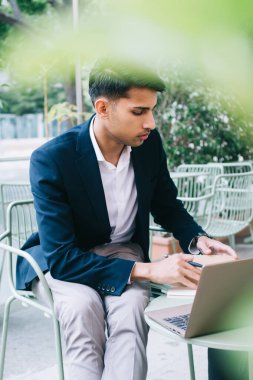 Ciddi yetenekli, modaya uygun resmi yönetici. Laptop bilgisayarla kafe terasında çalışıyor. Yakışıklı Hindu müreffeh iş adamı online projeden ve açık hava işinden memnun.