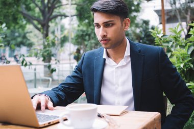 Ciddi ciddi gururlu erkek CEO çevrimiçi haberleri okuyor ve dışarıda dizüstü bilgisayarda postaları kontrol ediyor, modaya uyan zengin Hindu işadamı terasta uzaktan kumandalı bir işte video izliyor.