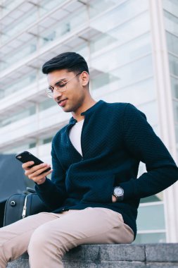 Milenyum sosyetesinden başarılı bir erkek hippi cep telefonuyla haber okuyor. Meydanda valiz çantasıyla oturuyor, Hindu giyinmiş bir adam şehir merkezinde akıllı telefondan uygulamayla internetten sohbet ediyor.