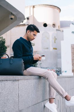 Moda kıyafetleri içinde ciddi Hindu erkek gezgin. Şehir merkezindeki uygulamalar üzerinden yeri aramak için cep telefonu kullanıyor. Yakışıklı 20 'li yaşlarda erkek turist akıllı telefonları kontrol ediyor.