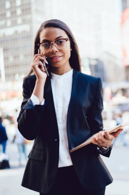 Başarılı Afro-Amerikan işkadını yarım uzunluk portre smartphone ayakta şehir üzerinde iletişim siyah takım elbise giymiş. Formal giyim cep üzerinde arama içinde müreffeh kadın emloyee