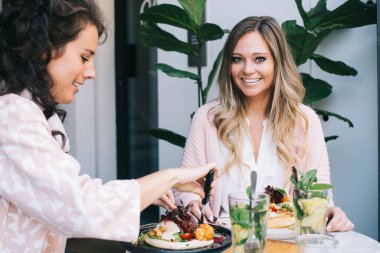 Gülümseyen sarışın kadın kameraya bakıyor. Esmer kadın en iyi arkadaşıyla yemekte olumlu bir konuşma yapıyor. Kafkasyalı hippi kız öğle tatilini kafede sağlıklı bir yemekle birlikte geçiriyor.