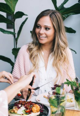 Gülümseyen beyaz tenli esmer ve sarışın kadınlar kafede oturmuş birbirleriyle konuşuyorlardı. Menüden sağlıklı yemekler yiyorlardı. Neşeli bayan arkadaşlar yemeğin tadını çıkarıyorlardı.