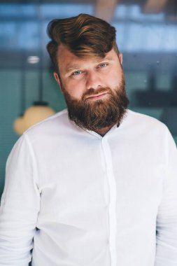 Yarım boy erkek sakallı iş adamı portresi, beyaz şık gömlekli, marka adı için fotokopi alanı olan, kendine güvenen beyaz erkek girişimci, modern çalışma alanında 30 'lu yaşlarda poz veriyor.