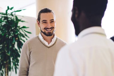 Çalışma grubunun koyu tenli erkek lideri, çalışanlarıyla iş birliği hakkında konuşuyor, gülümseyen kadın ve erkek çalışanlar ofis içindeki dostane atmosferden memnun.