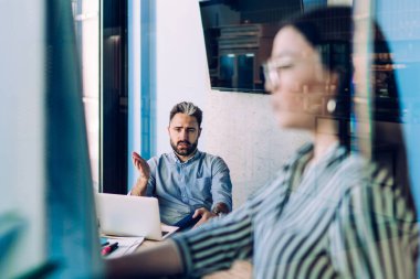 Düşünceli erkek, şirket ofisinde eğitim görürken dizüstü bilgisayarla masada oturuyor ve meslektaşını sorguluyor.