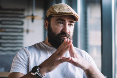 40 'lı yaşlarda rahat bir erkek kafenin penceresinde oturmuş fikir ve planlar üzerinde kafa yoruyor, ciddi sakallı yetişkin bir adam kafenin içinde boş zamanlarını değerlendiriyor.