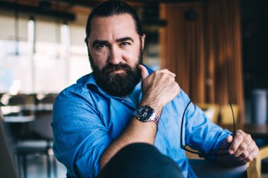 Kafenin içindeki dizüstü bilgisayarda uzaktan çalışan kendinden emin, sakallı bir girişimci. Kafkasyalı ciddi bir iş adamının uzaktaki serbest iş yaparken kameraya baktığı portre.