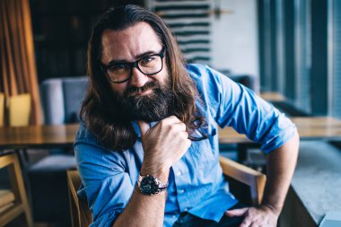 Uzaktan çalışma sırasında kafenin içinde oturan beyaz sakallı bir adamın portresi. Zengin, yakışıklı, 40 'lı yaşlarda erkek. Dizüstü bilgisayarda serbest çalışmaktan memnun bir şekilde kameraya bakıyor.