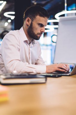 Yüksek hızlı internet bağlantısı ile birlikte çalışma alanında oturan, serbest çalışan yetenekli beyaz adam yazı yazma kursu, erkek akıllı günlük izleme kursu ve taşınabilir dizüstü bilgisayarla uzak mesafe işi