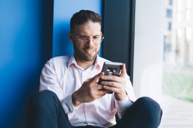 Optik gözlük takan mutlu erkek blogcu sosyal ağlardan sanal takipçilerle göz koruması sağlıyor, cep telefonuna içerik metni yazan neşeli bir adam