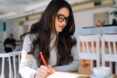 Gözlüklü genç ve çekici bir yazar kafeteryada otururken not defterinde yeni bir makale yaratıyor, üniversite sınavına hazırlanırken kapalı alanda sorulan sorulara cevap düşünüyor.