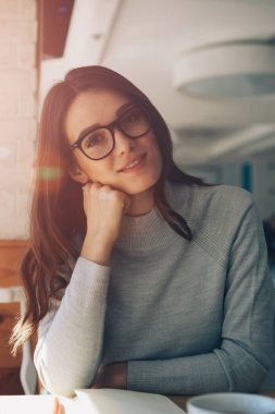 Güneşli bir günde evde oturup eğlenen gülümseyen genç kız portresi, kafeteryada dinlenip ara verdiğimizde kameraya bakan gözlüklü mutlu kadın.