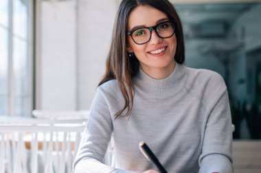 Kafeteryada eğlenen ve mola sırasında kameraya bakan gazeteci olarak çalışan neşeli hipster kız, başarılı mutlu yazar birlikte çalışma alanında otururken yeni roman fikirleri yaratarak