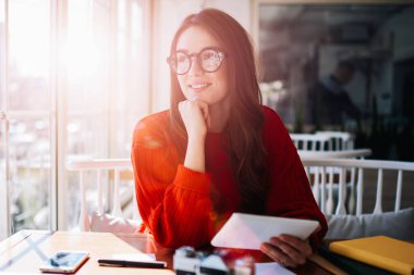 Gözlüklü mutlu bir kadın modern dokunmatik dokunaçları elinde tutuyor başarılı gülümseyen hippi kız kafeteryada dinlenirken ve okurken gözlerini kaçırıyor teknoloji ve iletişim kavramı.