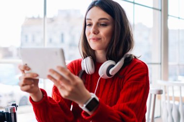 Dijital tablette oyun oynayan konsantre hipster kafeteryada otururken ve kablosuz internet alanına bağlanırken, mutlu genç kız arkadaşıyla taşınabilir bilgisayar kullanarak video sohbeti yapıyor.