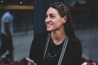 Moda pozitif kız öğrenci elinde cep telefonuyla bankta otururken not defteri ve kahve yanında kalıyor, mutlu kadın gülümsüyor ve yüzünü çevirmiş cep telefonundan son durumu bildiriyor.