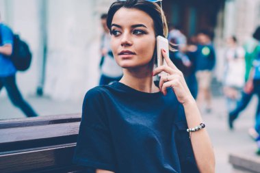 Güzel görünümlü hippi kız, akıllı telefon uygulamasını arama için kullanmaktan bahsederken düşünceli bakışlarını kaçırıyor. Açık havada cep telefonuyla iletişim kuran düşünceli çekici bayan turist.