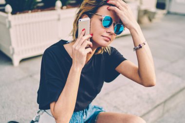 Moda bir bayan gezgin modern akıllı telefon ve 4G internet kullanarak turistik bilgileri arıyor. Güneş gözlüklü yeniyetme kız dışarıda cep telefonuyla sohbet ediyor.