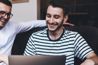 Dizlerinin üzerinde dizlerinin üzerinde oturmuş, kanepede oturmuş gülüp eğlenen zeki, şık ve neşeli genç adamlar.