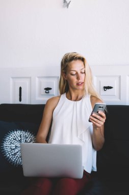 Barcelona 'da modern oturma odasında dizüstü bilgisayarla çalışırken gündelik kıyafet giyen zeki sarışın bayan girişimci.