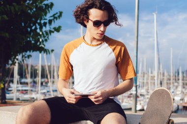 Güneş gözlüklü şık, kıvırcık saçlı adam. Güneşli bir günde Barcelona 'da kaykay yaptıktan sonra cep telefonuyla dinleniyor.